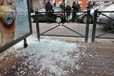 Policial olha para vidro quebrado no ponto de bonde, após a captura de suspeito de ataques em Bruxelas, enquanto a equipe de uma emissora local capta imagens. (Foto: Reuters)