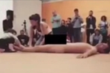Criança de cerca de quatro anos (esquerda) é estimulada por mulher adulta (centro) a tocar corpo nu do homem que está deitado no tablado durante performance do '35º Panorama da Arte Brasileira – 2017'. (Imagem: Reprodução - Internet)