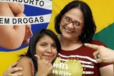 Damares Alves (direita) e Lulu (esquerda) abraçadas em frente à bandeira de uma campanha contra o aborto. (Foto: Instagram)