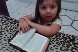 Ajoelhada em frente a uma cama, com os braços apoiados sobre uma Bíblia, a menina inicia suas preces. (Foto: Reprodução)