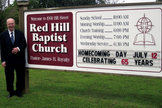 James Royalty ao lado da placa da Igreja com o anúncio de seus 65 anos de pastoreio, em 2015. (Foto: Reprodução/Baptist Red Hill Church)