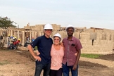 Darryl e Shirley Peters e auxiliar do casal, na Tanzânia; ao fundo, construção do centro de saúde. (Foto: Reprodução / CHVN Radio)