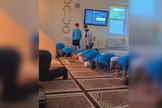 Jovem permanece em pé enquanto os demais participantes se ajoelham durante oração islâmica em mesquita. (Captura de tela/X/@megbasham)