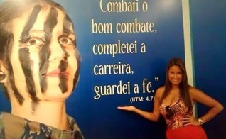 Drielle diante de mural com versículo: "Combati o bom combate, completei a carreira, guardei a fé". (Jornal Atual Rio)