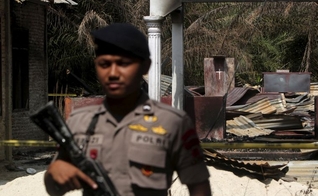 Policial segura rifle enquanto fica de guarda em frente a uma igreja queimada em Suka Makmur Village, em Aceh, Indonésia