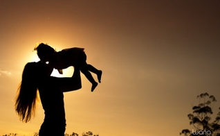 Mãe levanta a filha nos braços durante um por do sol. (Foto: Luana Okaeda)