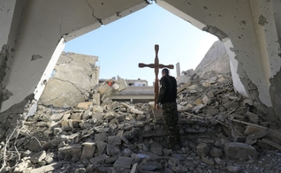 Um membro das forças árabes-curdas da Síria coloca uma cruz nos escombros antes de uma celebração de Natal na Igreja Católica Armênia dos Mártires, no centro da cidade de Raqa, leste da Síria, em 26 de dezembro de 2017. (Foto: DELIL SOULEIMAN / AFP)