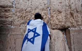 Jovem durante oração no Muro das Lamentações, coberto com a bandeira de Israel. (Foto: Reuters/Darren Whiteside)