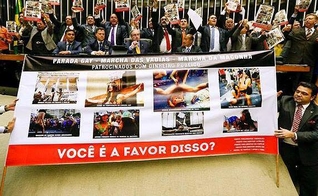 Deputados Evangélicos e católicos expõem cartazes com imagens de protestos que ofenderam o cristianismo, com a profanação de ícones religiosos.