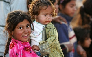 Garota síria segura bebê no colo, em campo de refugiados. 