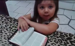 Ajoelhada em frente a uma cama, com os braços apoiados sobre uma Bíblia, a menina inicia suas preces. (Foto: Reprodução)