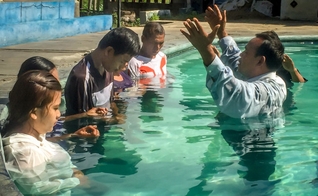 Pastor faz oração durante batismo de novos convertidos, em país da Ásia. (Foto: Christian Aid Mission)