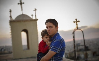 Homem cristão segurando seu filho, enquanto muitos de seus vizinhos fugiram da violência no Iraque. (Foto: Warrick Page/New York Times)