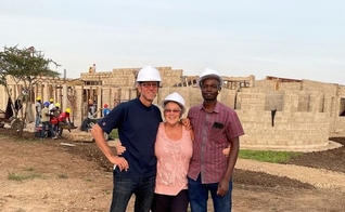 Darryl e Shirley Peters e auxiliar do casal, na Tanzânia; ao fundo, construção do centro de saúde. (Foto: Reprodução / CHVN Radio)