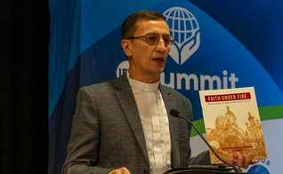 Pr. Mykhailo Brytsyn segurando o relatório “Fé sob Fogo” enquanto fala sobre sua experiência na guerra russa contra a Ucrânia. (Foto: Christian Daily International)