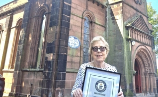 Pam Knowles em frente à igreja segura sua placa do Guinness Book. (Foto: Facebook/St. Anne’s, Aigburth)