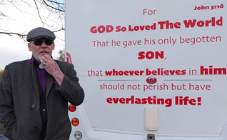 Pastor Mick Fleming ao lado de sua van, que traz o versículo bíblico João 3:16. (Captura de tela/YouTube/Church on the Street Ministries)