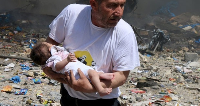 Homem segura bebê sobrevivente a bombardeio com barris explosivos em Aleppo. (Abdalrhman /Reuters)