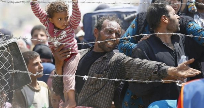 Refugiado sírio segura sua filha, enquanto tenta cruzar a fronteira da Turquia (Foto: Reuters)