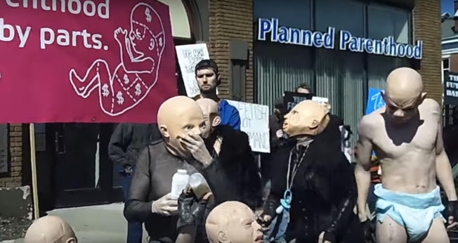 O protesto foi realizado por satanistas que se vestiram de "bebês sadomasoquistas". (Foto: Reprodução/YouTube)