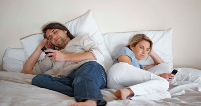 Casal usando celulares na cama. (Foto: Getty)