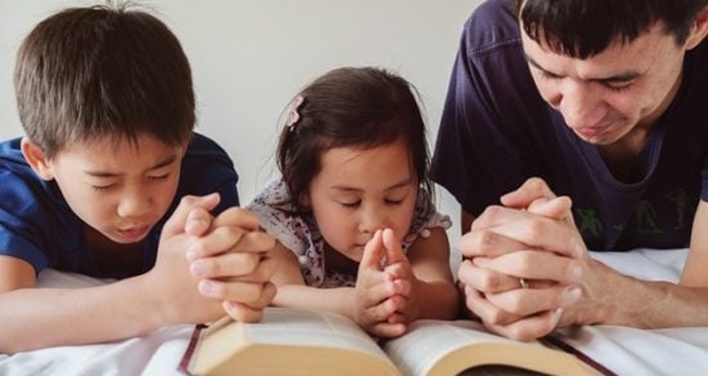 Pai lê a Bíblia com filhos. (Foto: Getty)