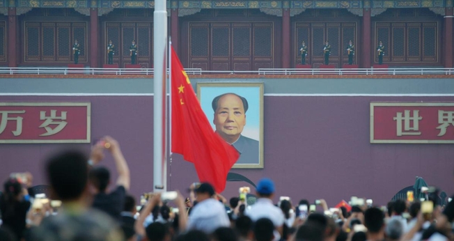 Visitantes acompanham uma cerimônia de hasteamento da bandeira com a imagem de Mao Tsé Tung ao fundo, na praça Praça da Paz Celestial, em Pequim, em julho de 2018. (Foto: CHINA STRINGER NETWORK/REUTERS/Newscom)