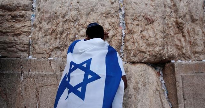 Jovem durante oração no Muro das Lamentações, coberto com a bandeira de Israel. (Foto: Reuters/Darren Whiteside)