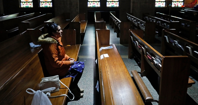 Mulher sentada no banco de uma Igreja Católica vazia em Des Moines, em Iowa, nos EUA. (Foto: Charlie Neibergall/Associated Press)