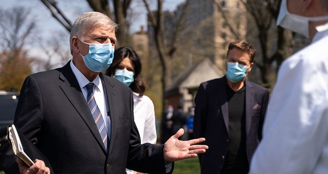 Usando máscaras, Pastor Franklin Graham (esquerda) é acompanhado do cantor Michael W. Smith (ao fundo) durante visita ao hospital de campanha montado pela Samaritan's Purse, organização missionária comandada pelo evangelista. (Foto: Samaritan's Purse)