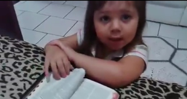 Ajoelhada em frente a uma cama, com os braços apoiados sobre uma Bíblia, a menina inicia suas preces. (Foto: Reprodução)