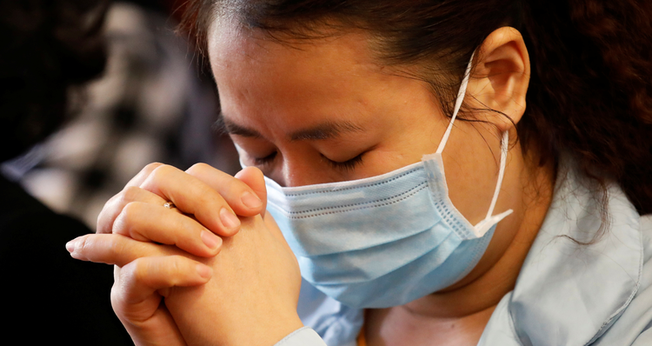 Uma mulher usa máscara enquanto ora em meio ao surto de coronavírus. (Foto do CNS / Kham, Reuters)