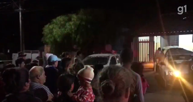 Enquanto os corpos eram retirados, os vizinhos oraram o Pai Nosso em frente a casa. (Foto: Reprodução/g1).