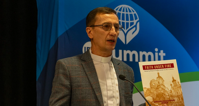 Pr. Mykhailo Brytsyn segurando o relatório “Fé sob Fogo” enquanto fala sobre sua experiência na guerra russa contra a Ucrânia. (Foto: Christian Daily International)