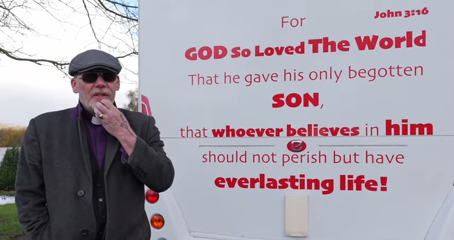 Pastor Mick Fleming ao lado de sua van, que traz o versículo bíblico João 3:16. (Captura de tela/YouTube/Church on the Street Ministries)