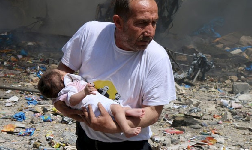 Homem segura bebê sobrevivente a bombardeio com barris explosivos em Aleppo. (Abdalrhman /Reuters)