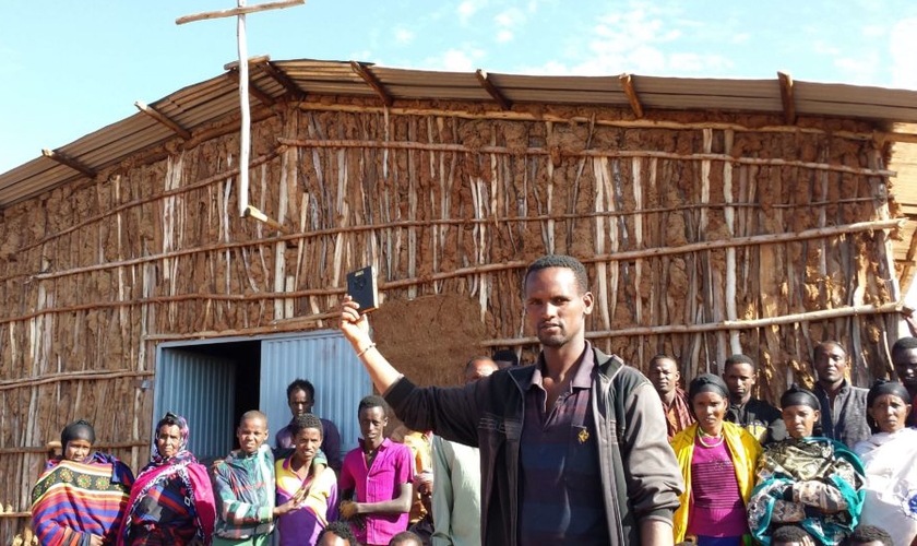 Em frente à igreja na África, cristãos seguram aparelho da Bíblia em áudio. (Foto: GHI)