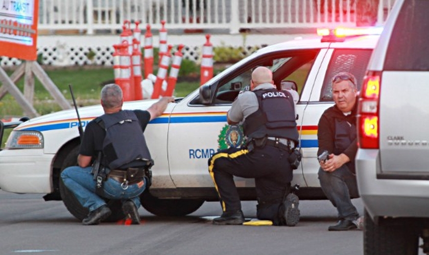 Agentes da polícia se escondem atrás de seus veículos em busca do atirador que teria matado policiais no Canadá 
