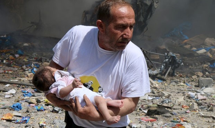 Homem segura bebê que sobreviveu a bombardeio com barris explosivos em Aleppo.