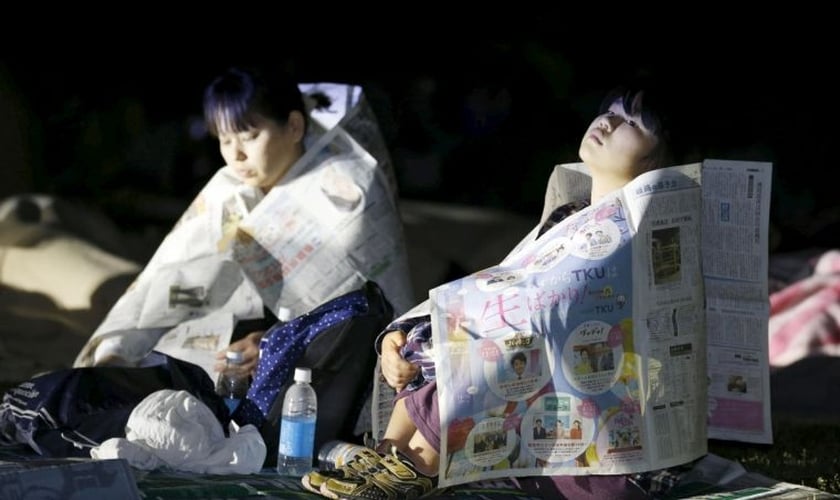 Sobreviventes do terremoto usam jornais para se aquecer, enquanto não são levadas pelas equipes de resgate. (Foto: Reuters)
