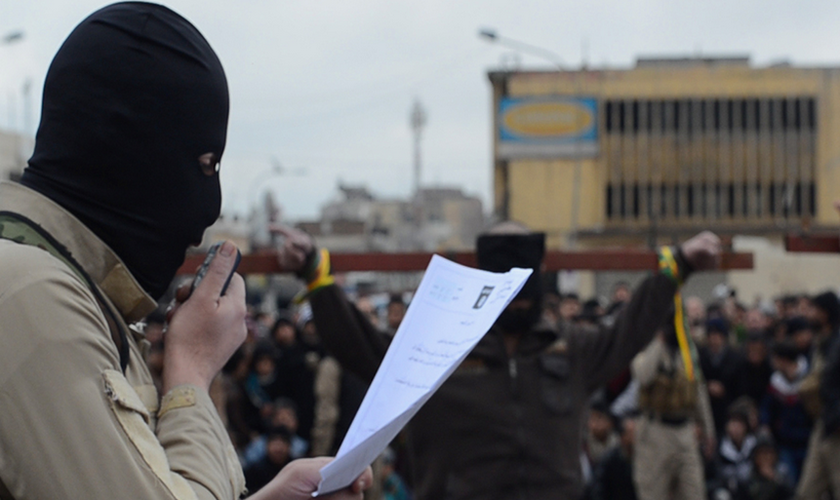 Terrorista do Estado Islâmico lê sentença de 'espiões' durante a crucificação dos mesmos. (Imagem: Captura de Tela)