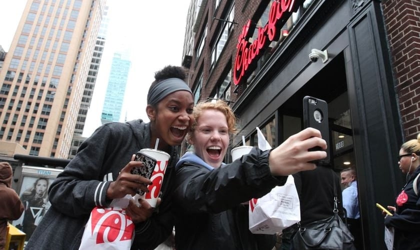 A jovem Jaimie Cranford (à direita) tira uma selfie com Mariah Reives (esquerda), exibindo sorrisos e seus lanches da rede lanchonetes fundadas por cristãos. (Foto: Tina Fineberg / AP Photo)