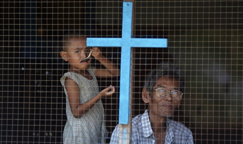 Homem e criança de família cristã olham pela janela de sua casa nos subúrbios de Yangon, em Myanmar. (Foto: Reuters/Damir Sagolj)