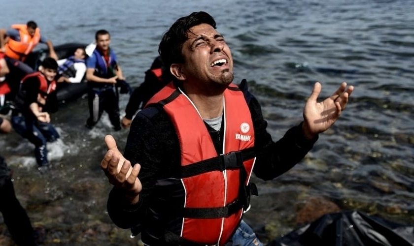 Homem ora após pisar em terra firme na ilha grega de Lesbos, depois de atravessar o mar. (Foto: Aris Messinis/AFP)