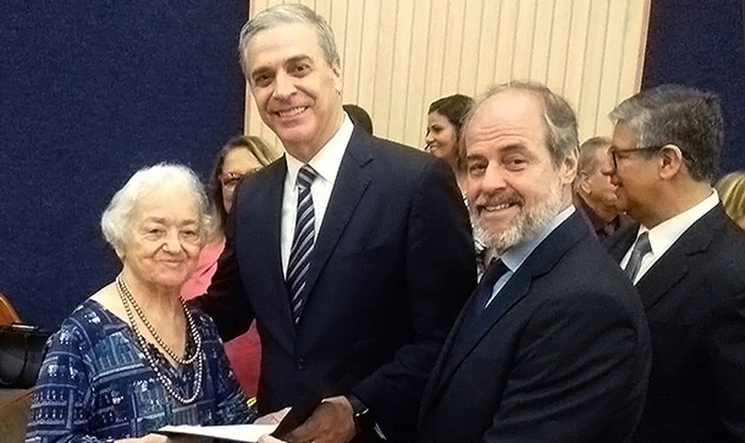 Maria Ribeiro recebe seu certificado de ordenação do Superintendente Geral David Busic e seu filho, Superintendente Distrital Elio Tomaz. (Foto: Divulgação/NCC News)