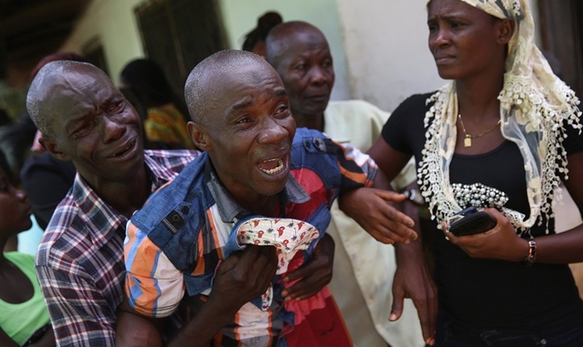 Liberiano chora enquanto o corpo de sua esposa é levado por uma equipe médica na África. (Foto: John Moore/Getty Images)