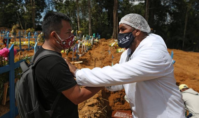 O pastor Izaías Nascimento conforta um jovem durante o funeral de seu pai. (Foto: Michael Dantas/AFP)