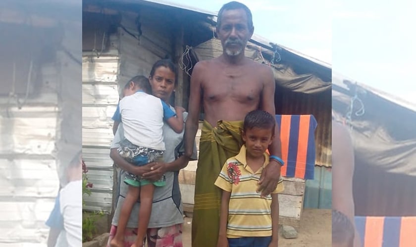 Khanjana ao lado da esposa e dois filhos, em frente à cabana da família. (Foto: Gospel For Asia)