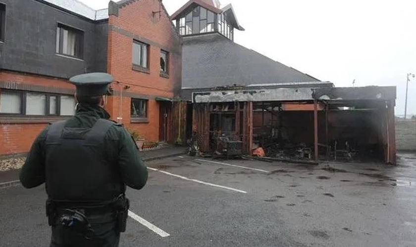 Policial observa igreja incendiada na Irlanda do Norte. (Foto: Reprodução / Bíblia Todo)