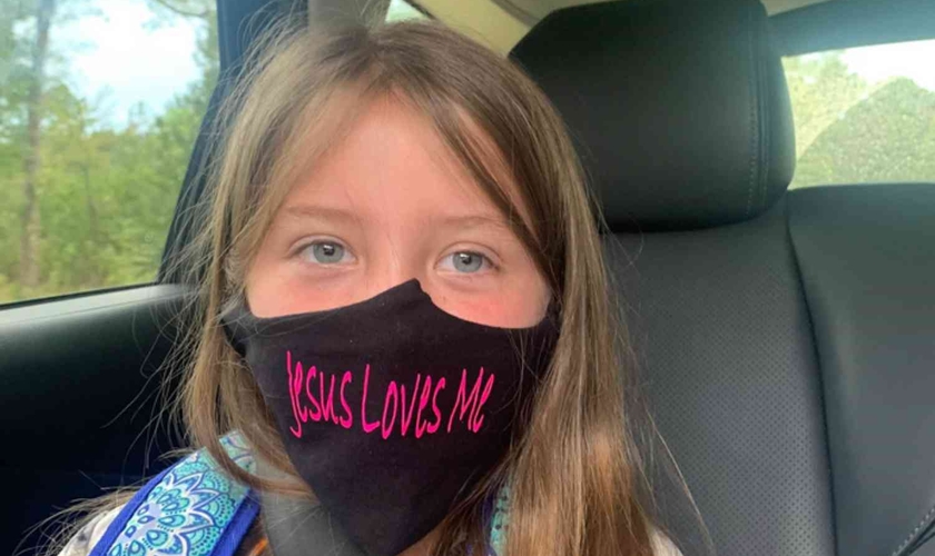 Lydia Booth foi proibida de usar sua máscara com a inscrição "Jesus Loves Me" ("Jesus me Ama") e agora sua família está processando a escola onde ela cursa a 3ª série. (Foto: Alliance Defending Freedom)